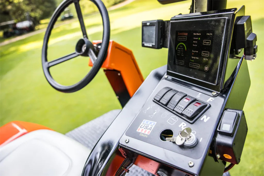 Control panel of Smithco Spray Star 1200 E featuring steering wheel, digital display, and operational controls for turf spraying.