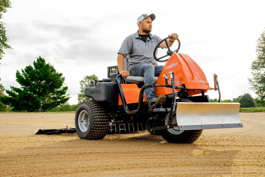 Man operating Smithco Sand Star Diesel Infield Groomer on sports field, showcasing advanced traction and hydraulic control features.